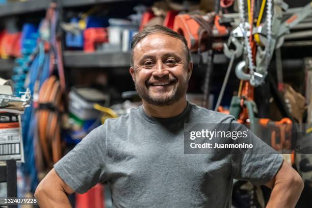 lächelnder hispanischer handwerker posiert in seinem geschäft mit all seinen werkzeugen, die in die kamera schauen - migrant worker stock-fotos und bilder