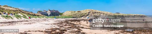northumberland people walking on bamburgh beach dunes panorama uk - beach shelter stockfoto's en -beelden