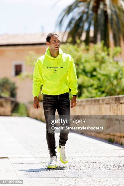 Marcel Remus wearing a neon yellow hoodie 'stay positive' by Marcel Remus Design, grey denim jeans by Marcel Remus Design and white and neon yellow...