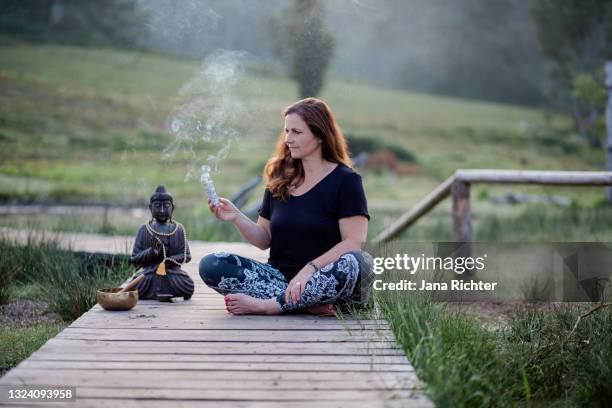 woman sits on a boardwalk and holds a lighted bundle of sage in her hand - lantana camara stock pictures, royalty-free photos & images