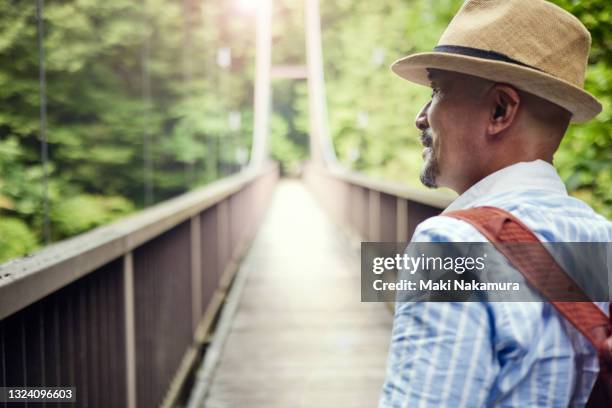 a senior man crossing a suspension bridge in the forest. - hängebrücke stock-fotos und bilder