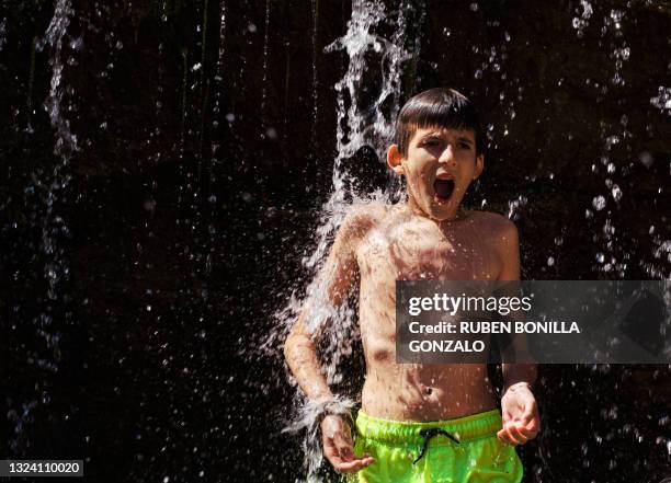 caucasian shirtless thin boy wearing a swimsuit having a shower in a waterfall of a thermal spa in nature on black background. - boy taking a shower stock-fotos und bilder