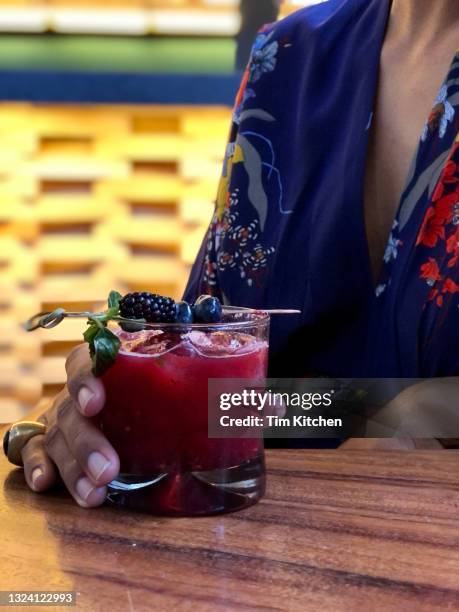 close up of a cocktail on a table, held by a woman's hand - blackberry fruit pattern stock pictures, royalty-free photos & images