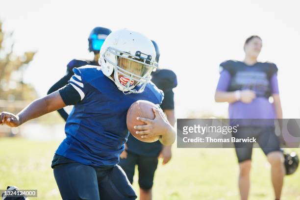 medium wide shot of young football player running with ball during game on fall afternoon - safety american football player 個照片及圖片檔