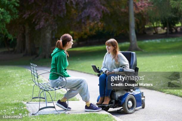 woman in wheelchair chatting with friend in park. - park bench stockfoto's en -beelden