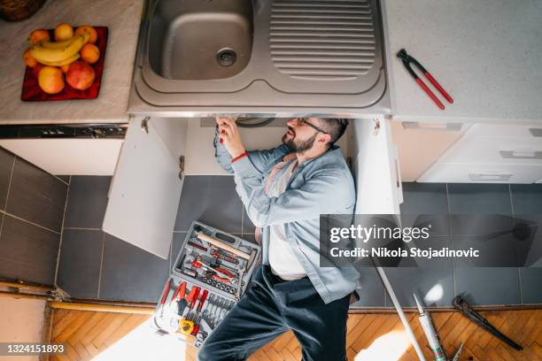 young repairman with tools in his hands is fixing the sink in the kitchen - fontein stockfoto's en -beelden