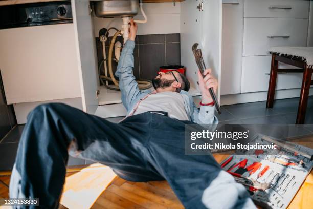 idraulico maschio che lavora per riparare il lavandino che perde - under sink foto e immagini stock