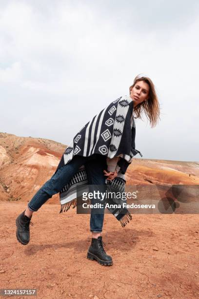 mountains without plants of different colors. mountains the color of mars. a tourist girl is walking in an unusual place. red earth. on the shoulders of the woman is a plaid with an ornament. - crazy holiday models stock-fotos und bilder