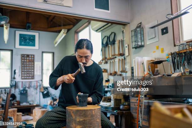 mid adult silversmith hammering silver in preparation for making jewellery - art smith stock pictures, royalty-free photos & images