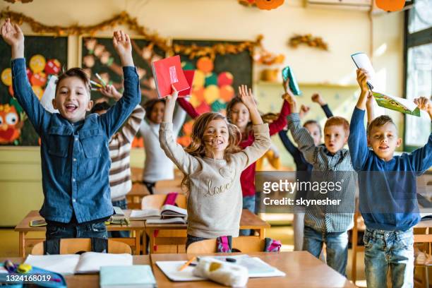 studenti elementari giocosi che saltano con le braccia alzate in classe. - the end foto e immagini stock