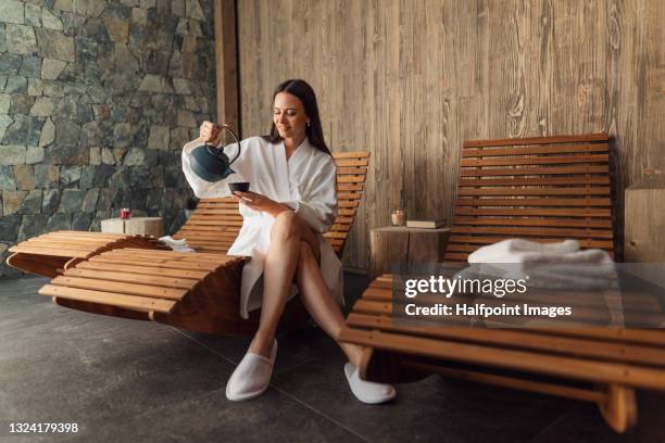 happy mid adult woman with bathrobe sitting in wellness resort, relaxing. - health spa foto e immagini stock