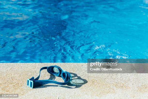 blue swimming goggles on the stone curb of the pool with blue water in the background. - schwimmbeckenrand stock-fotos und bilder