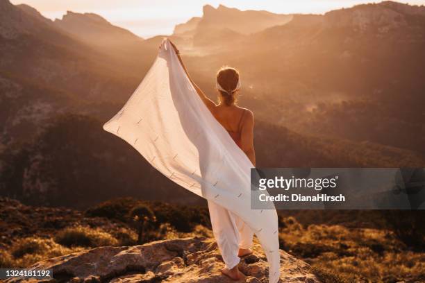 bella giovane donna da dietro che fa una danza cadente con uno scialle bianco durante l'alba in un paesaggio montuoso - scialle foto e immagini stock
