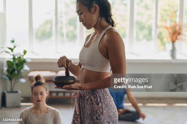 female asian yoga teacher conducting a meditation session with a singing bowl - rin gong 個照片及圖片檔