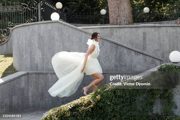 happy beautiful bride walks up the stairs - weißes kleid stock-fotos und bilder