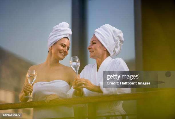 happy women with bathrobe and wine standing outdoors in wellness resort, relaxing. - mother daughter towel fotografías e imágenes de stock