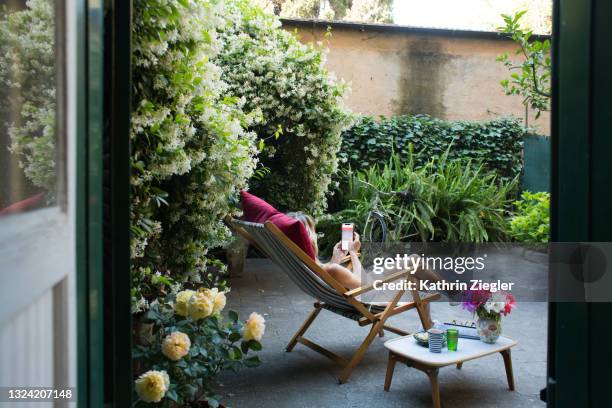 woman relaxing on deck chair in back yard, checking her phone - single rose ストックフォトと画像