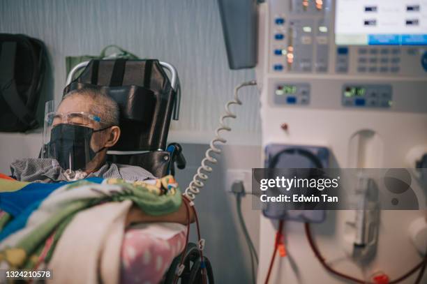 顔の盾を持つ車椅子のアジアの中国人の先輩男性、病院で透析治療の下でフェイスマスク - 生理食塩水 ストックフォトと画像