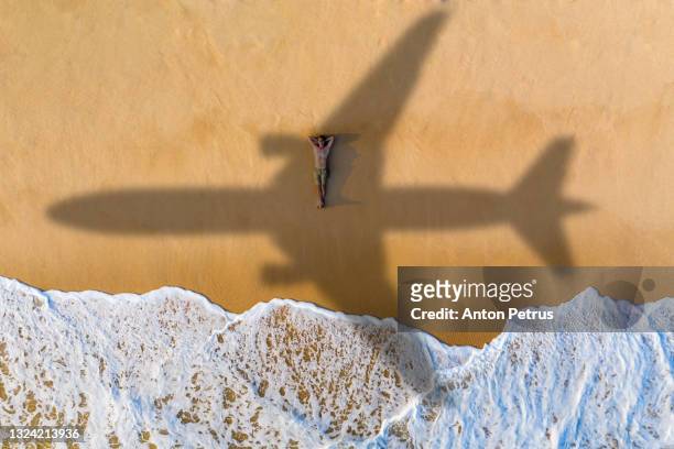 airplane silhouette over the guy on a sandy beach on a tropical island. travel and resort vacation concept - beach plane stock pictures, royalty-free photos & images