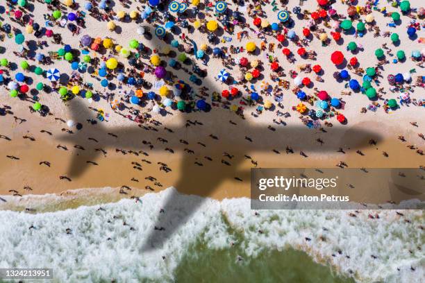 airplane silhouette over copacabana beach with beach umbrellas and sun loungers. rio de janeiro, brazil. - crowded airplane stock pictures, royalty-free photos & images