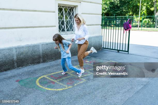 happy schoolgirl playing hopscotch with her mother on school playground outdoors - hopscotch stock pictures, royalty-free photos & images