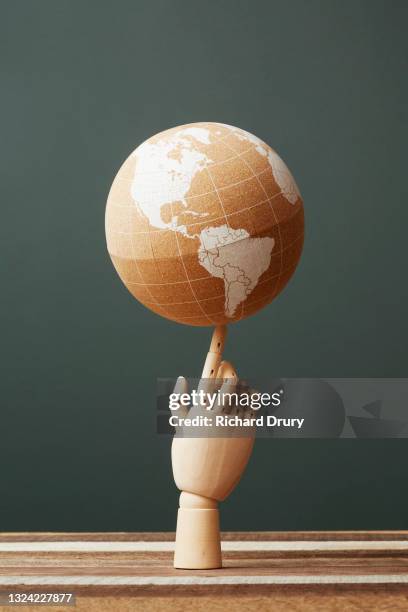 a world globe balanced on the finger of a wooden hand - artists model stock photos et images de collection