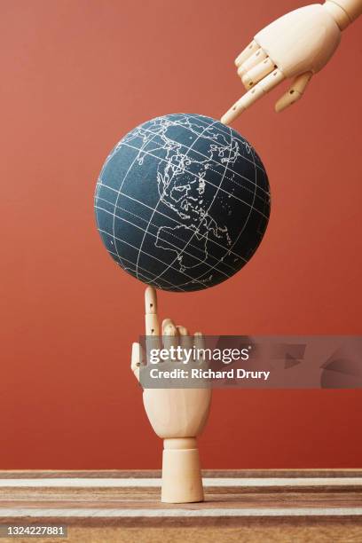 a world globe balanced between the fingers of two wooden hand - global stability stock pictures, royalty-free photos & images