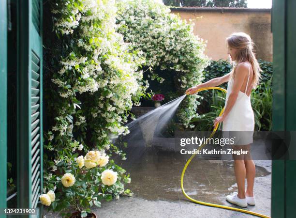 woman watering plants in back yard, wearing white summer dress - garden hose imagens e fotografias de stock