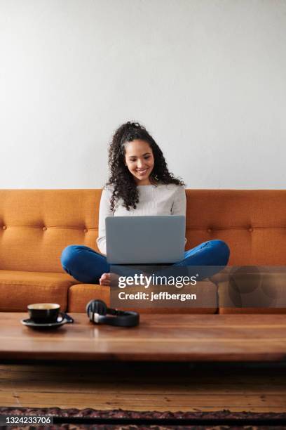 shot of a young female sitting on the couch and using her laptop at home - laptop couch stock pictures, royalty-free photos & images