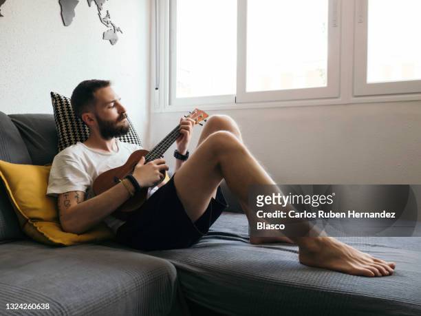 young man relaxing at home while playing music on his ukulele - ukulele stock-fotos und bilder