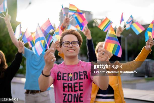 portrait of an lgbtq+ activist holding rainbow flags in his hands - gay flag stockfoto's en -beelden
