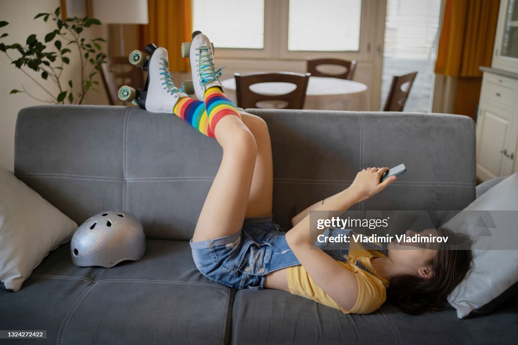 A teenager lyiing  down with her legs resting on the back of a sofa