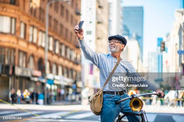 active senior taking selfie on bicycle in downtown district - crossing the road stock pictures, royalty-free photos & images