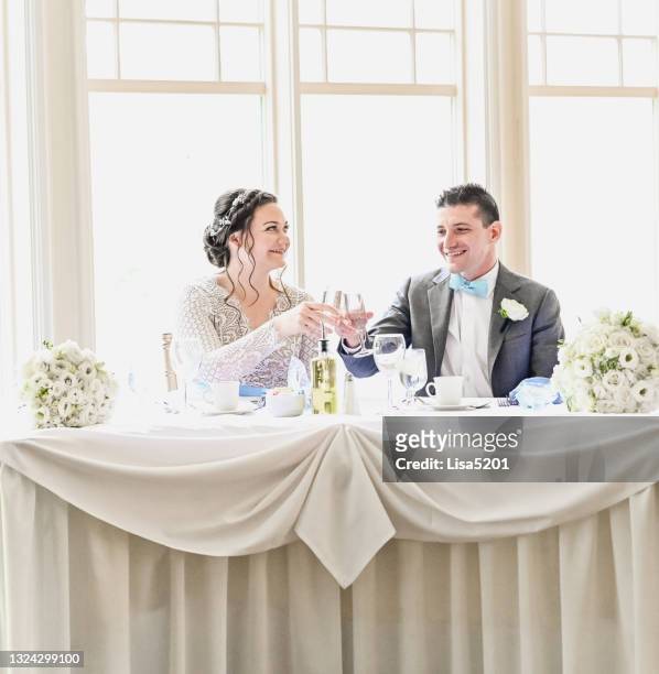 bride and groom cheers with champagne at the head table at their wedding reception - banquet hall stockfoto's en -beelden
