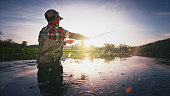 Fly fisherman stands in the water and casts the fly with fishing rod using Roll Cast with lot of splashes