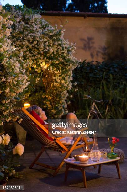 woman relaxing on deck chair in back yard, enjoying a glass of wine while listening to music - backyard deck stockfoto's en -beelden