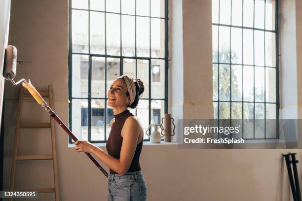 femme joyeuse peignant le mur avec rouleau de peinture - woman painting window photos et images de collection