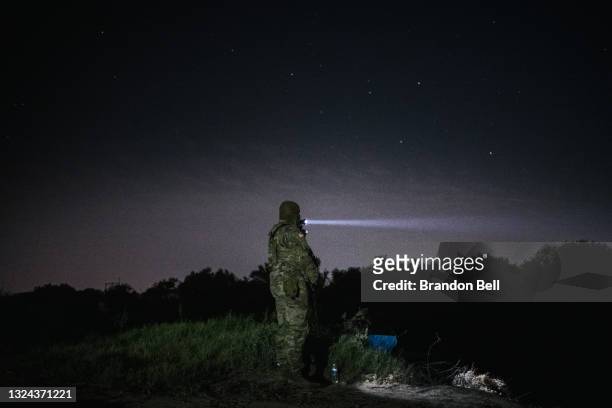 Member of the National Guard shines a flashlight across the Rio Grande on June 19, 2021 in Roma, Texas. A surge of mostly Central American immigrants...