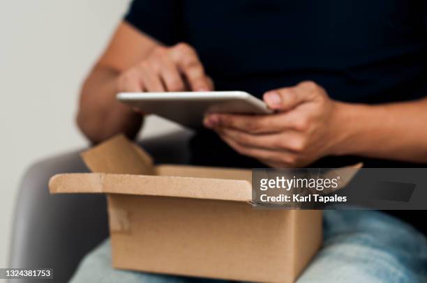 a southeast asian man is holding a carton box package and digital tablet - returning merchandise stock pictures, royalty-free photos & images