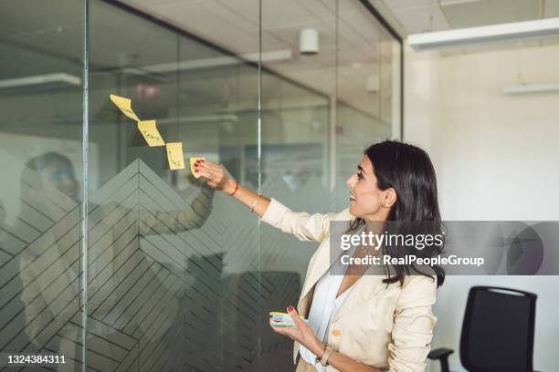 happy smile mid adult business woman. write a message and stick on a glass board. - scrummen stockfoto's en -beelden