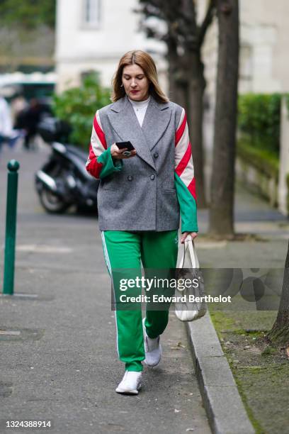 Guest wears a gold pearl earring, a pearl necklace, a white wool turtleneck pullover, a gray striped green white and red sleeves blazer jacket, an...