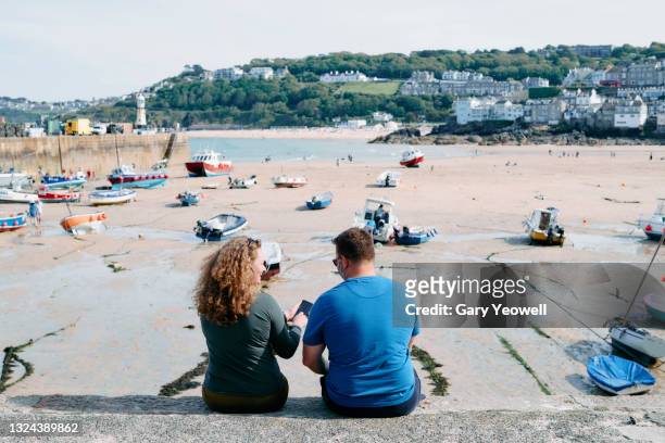 man and woman sitting on the harbour in st ives - st ives cornwall stockfoto's en -beelden