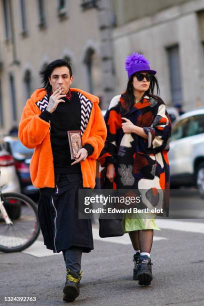 Guest wears black with red embroidery collar shirt, an oversized orange with black and white interior bomber fluffy coat, a long zipper cardigan,...