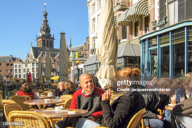 a young couple sits on a terrace at the grote markt in nijmegen, the netherlands. in the background the historic buildings of the grote markt, including the st stevenstoren. - nijmegen stockfoto's en -beelden