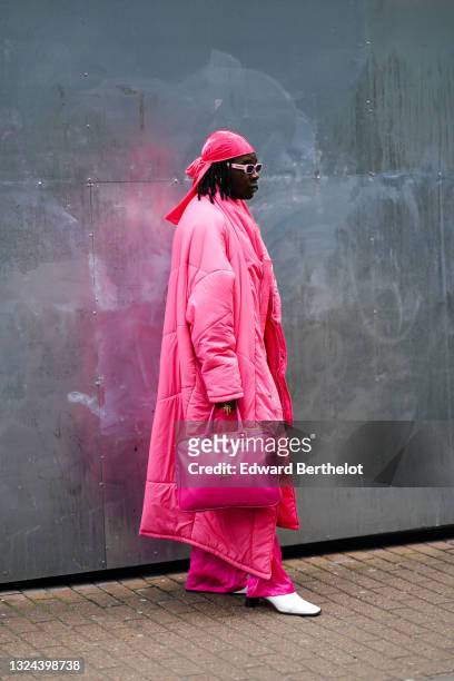 Guest wears a pink velvet hat, pale pink sunglasses, a long oversized pink puffer jacket, a fuchsia flared pants, white pointy heel ankle boots, a...