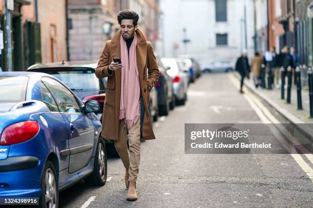 Guest wears a pink wool scarf, a black turtleneck pullover, a camel long trench coat, beige pants, a brown leather Hermes Double Tour gold logo...