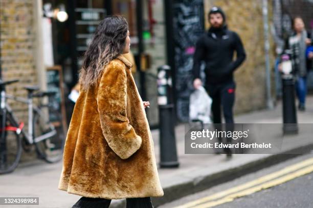 Guest wears a camel fluffy coat, a black ribs flared pants, during London Fashion Week Men's January 2020 on January 05, 2020 in London, England.