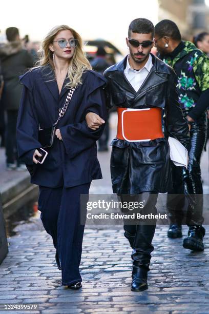 Guest wears blue sunglasses, pearls an rhinestones silver earrings, an oversized black stripes puffy shoulders long blazer jacket, navy blue denim...