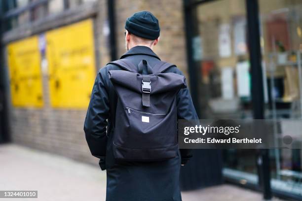 Guest wears a black beanie, a long black coat, a black backpack bag, during London Fashion Week Men's January 2020 on January 05, 2020 in London,...