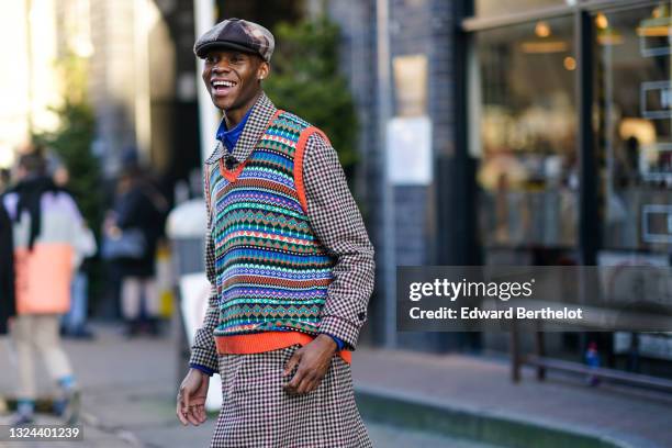 Guest wears a black and white and red checkered side and an houndstooth fabric side beret hat, a pearl earring, a bold blue zipper turtleneck...